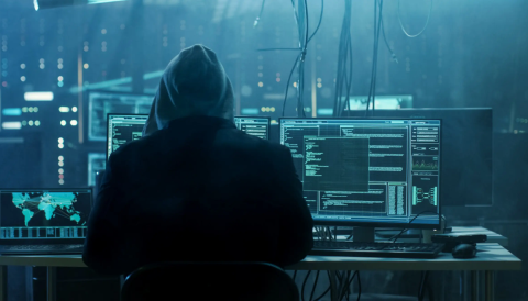 Hacker with hoodie from behind, facing computer screens